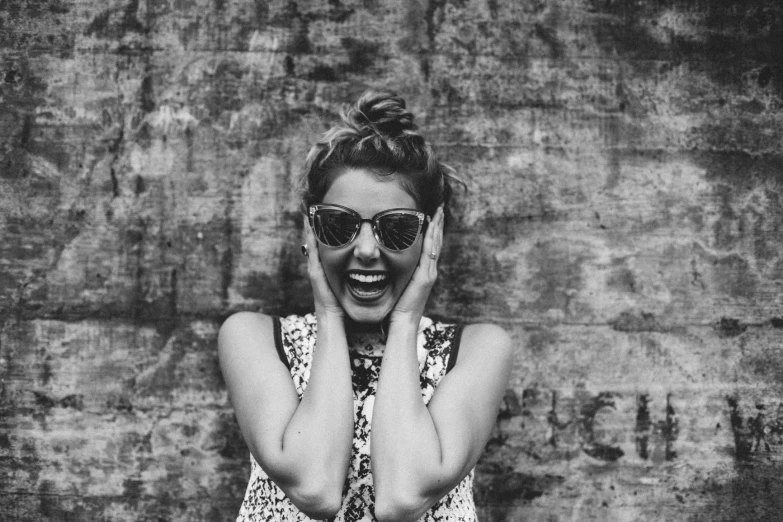 black and white pograph of a woman with sunglasses and her hands to her head