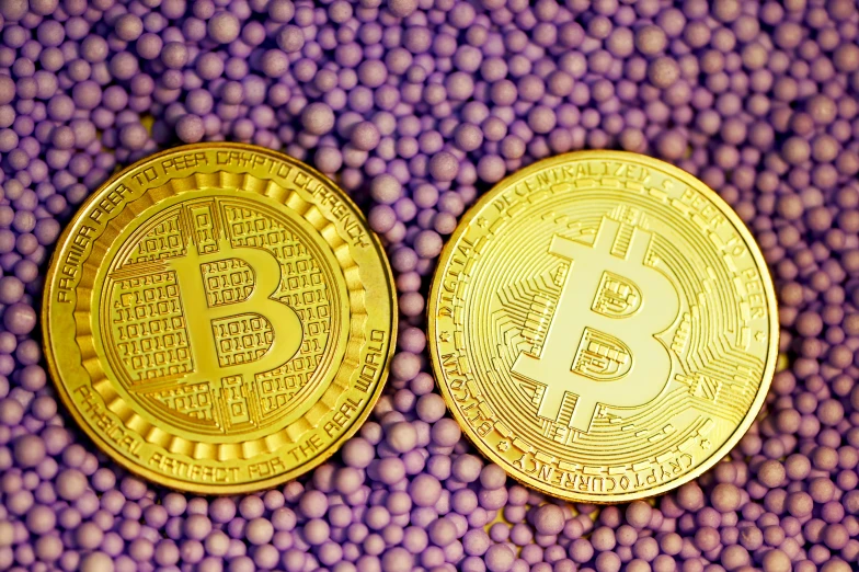 two golden bitcoins sitting on top of a purple surface