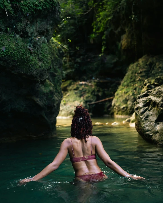 a woman wearing a bikini sitting in water near a rocky cliff