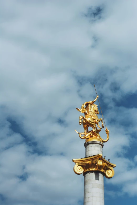 statue with gold detailing on top of building against cloudy sky