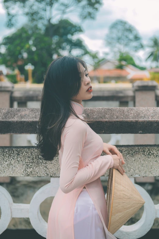 a woman in pink dress leaning on a fence