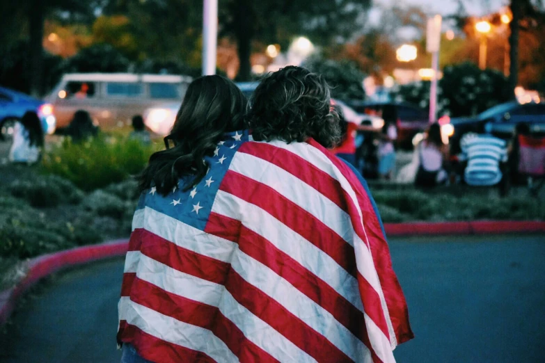 two people wrapped in a usa flag on top of a street
