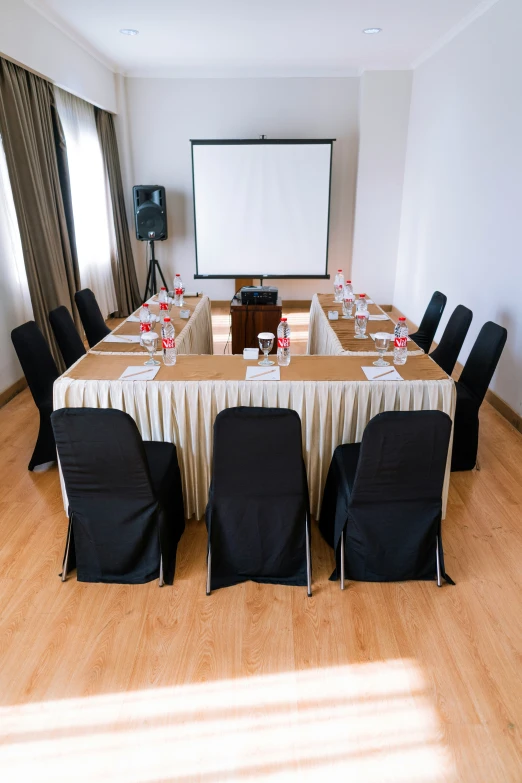 a long table with chairs on each side of it with a projector screen behind it