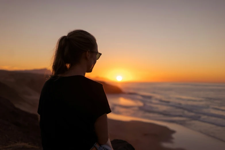 a woman looks into the distance as the sun sets