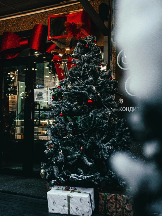 a lit christmas tree next to presents in front of a building