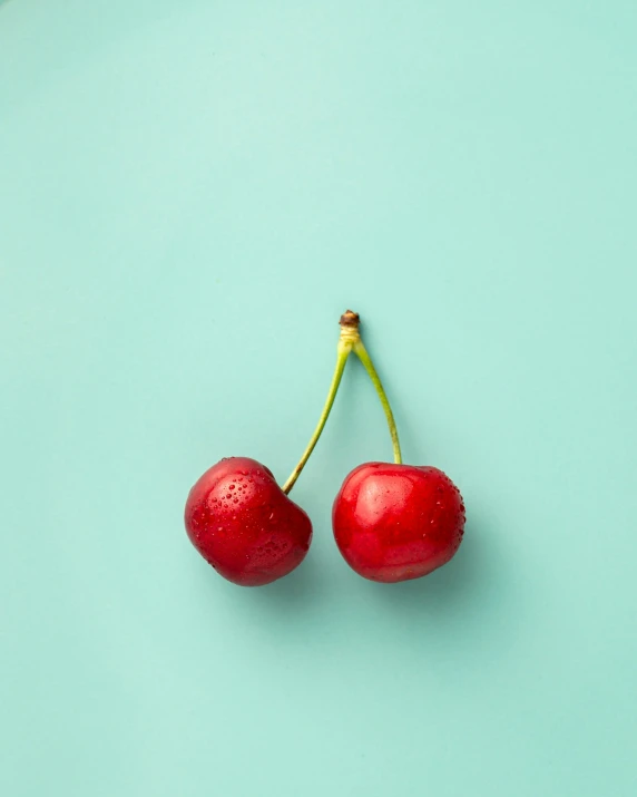 two cherries are sitting on a green surface