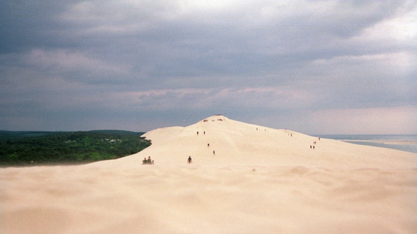 several people walking on top of a very large sand mountain