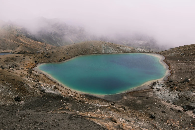 a blue lake is surrounded by mountains on a foggy day