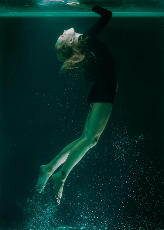 a girl wearing green pants and black top is diving under water