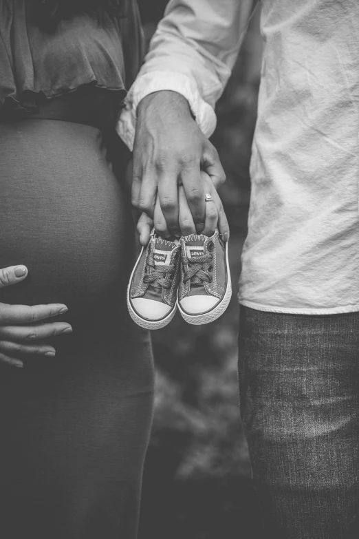 a pregnant woman's hand is held by her husband, who wears shoes