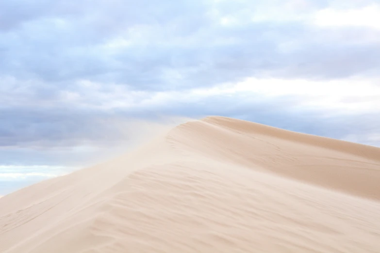 there are clouds in the sky over a very large sand dune