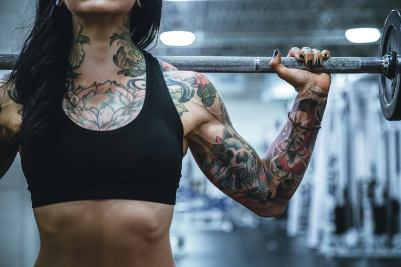 a tattooed woman lifting a barbell in the gym