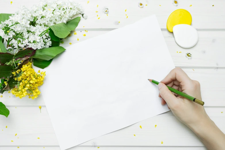 someone is drawing on a paper on the table with flowers