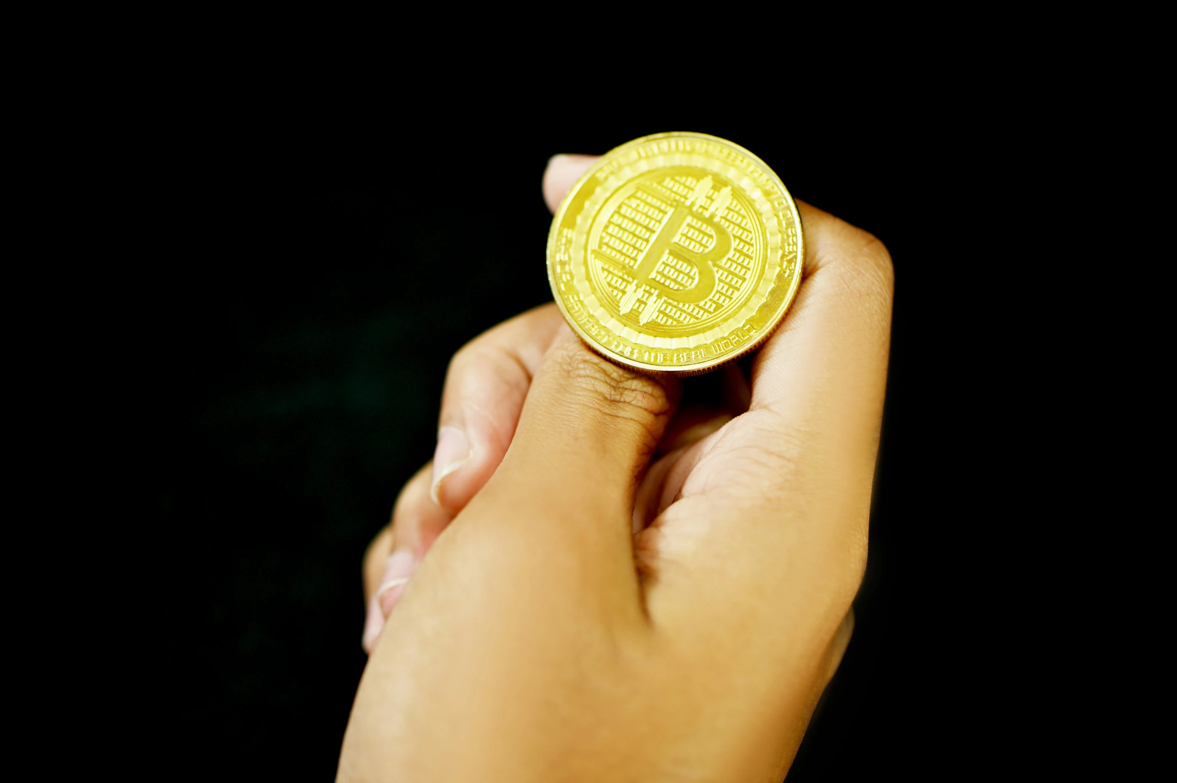 a person holding a golden bit coin in their hand