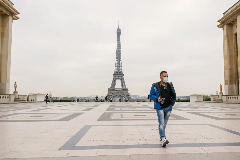 a man walking in front of the eiffel tower with a mask on