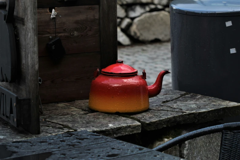 a red teapot sitting on the ground near a trash can
