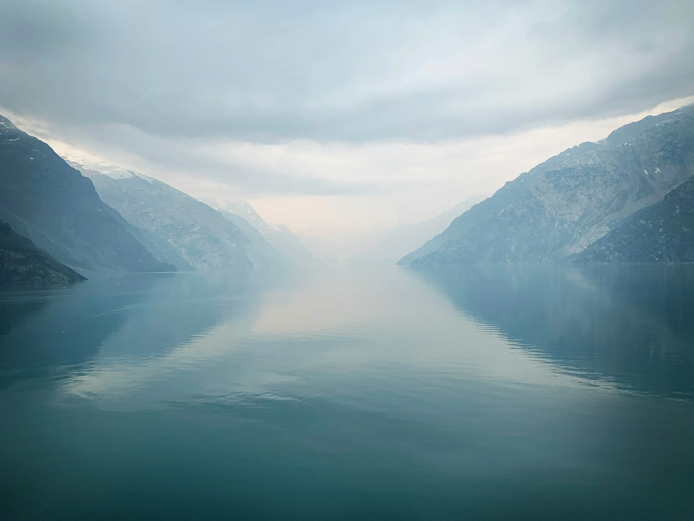 a body of water surrounded by mountains on a cloudy day