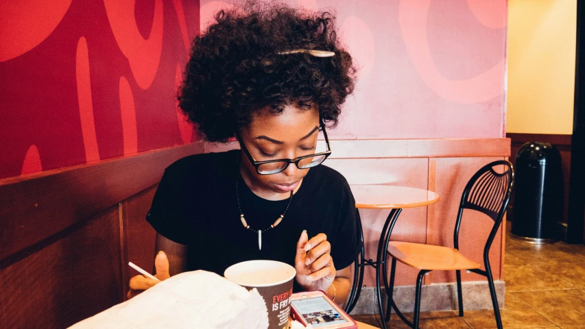 a woman is looking at her phone and writing on a book