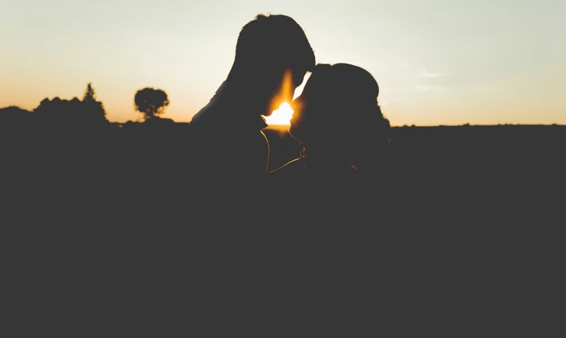 two people kiss on the cheek with the sun in the background