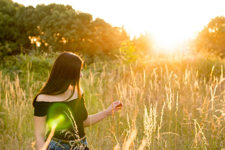 a woman is walking through tall grass towards the sun