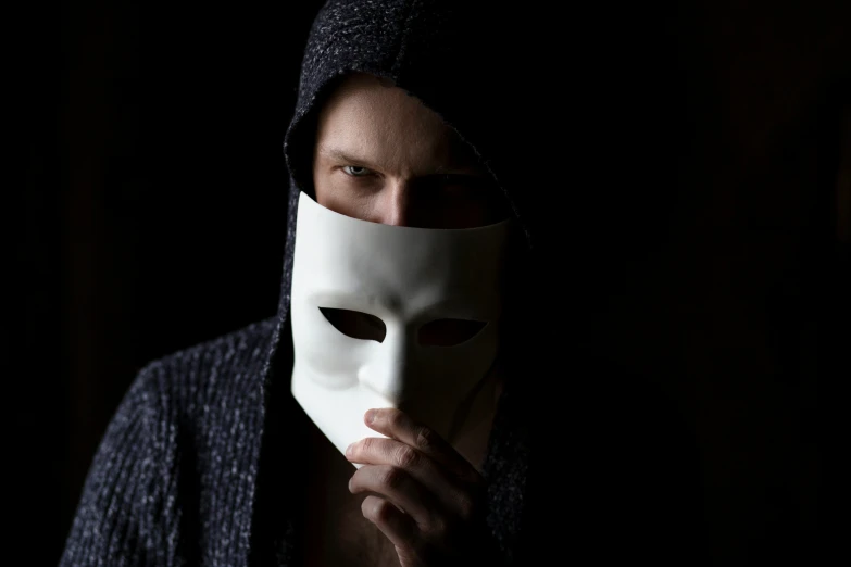 a man in a black coat is holding a white mask