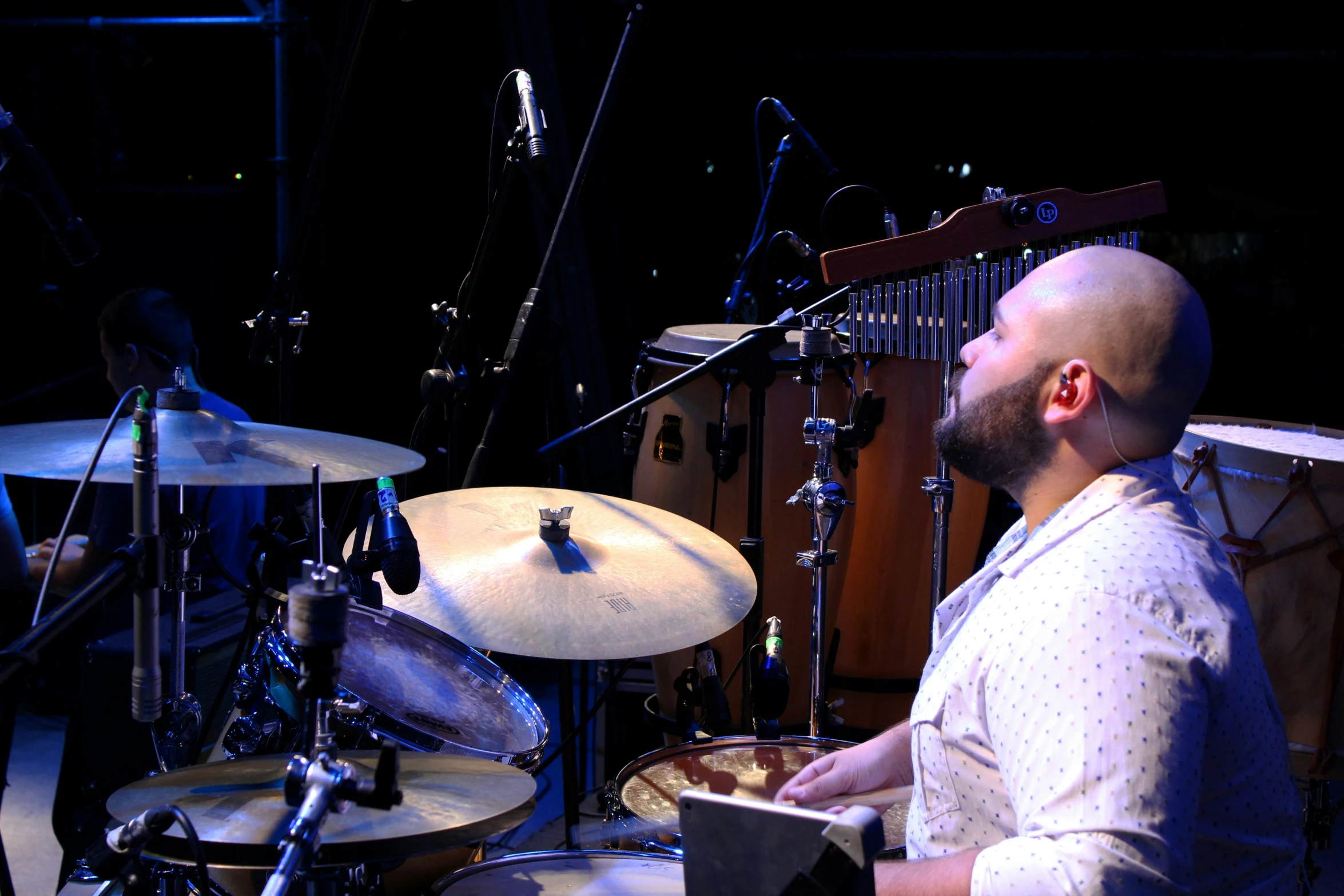 a man with a beard and a bald head sitting in front of a drum set