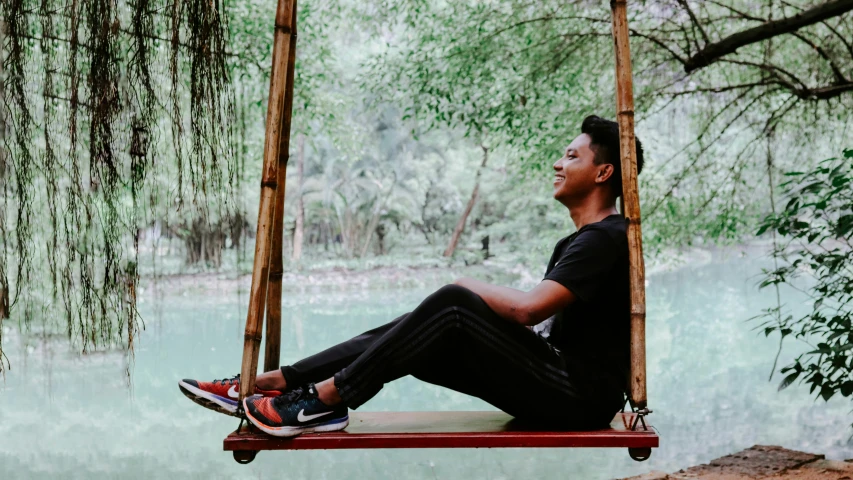 man sitting on a swing in front of some water