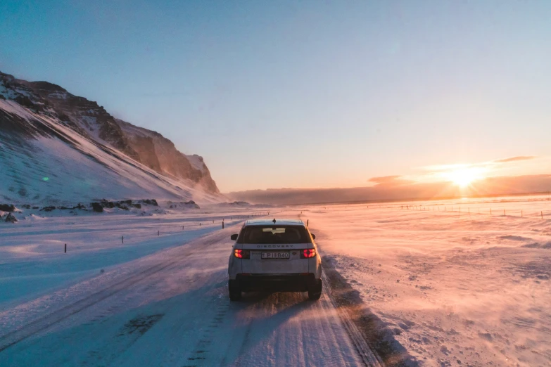 a car driving down the road near mountains at sunset