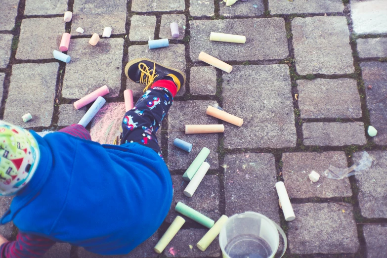 a little  standing on top of sidewalk covered in crayons