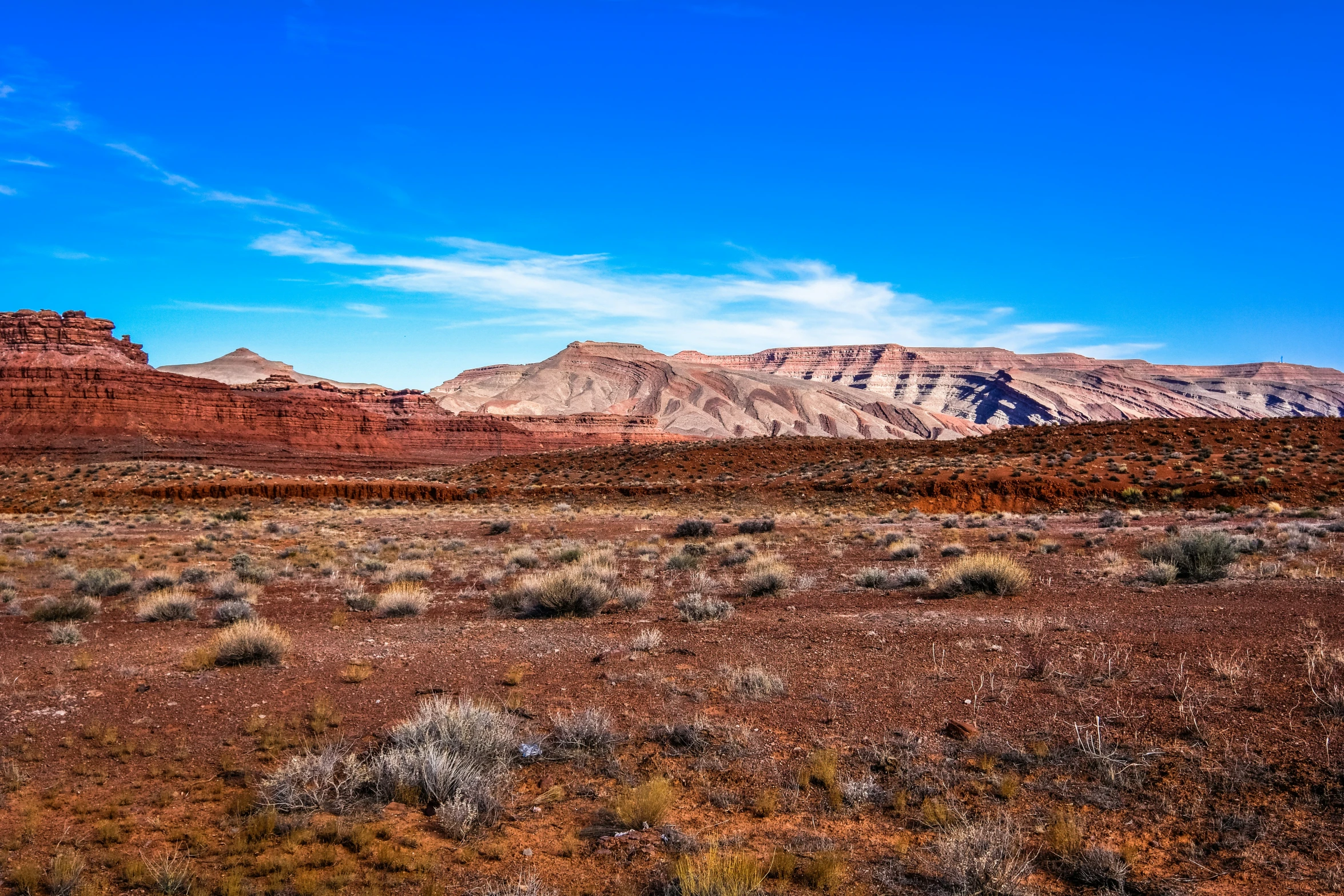 mountains and desert with shrubs around them, under a blue sky