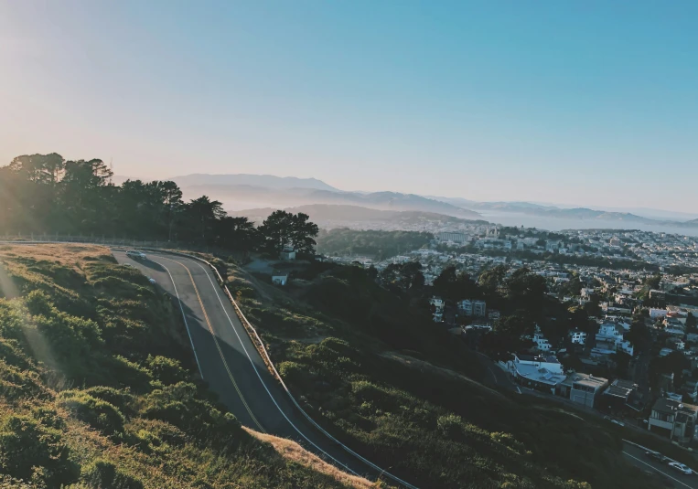 a car driving down a hill with trees and hills around