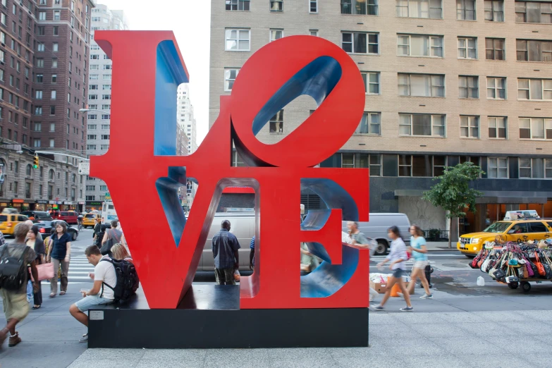 people walking around a large art piece that says love