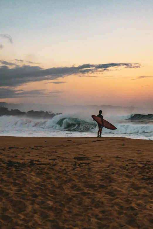 surfer in wetsuit standing on the beach holding his surfboard