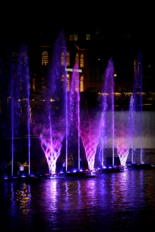 a nighttime scene shows several colorful fountains lit up
