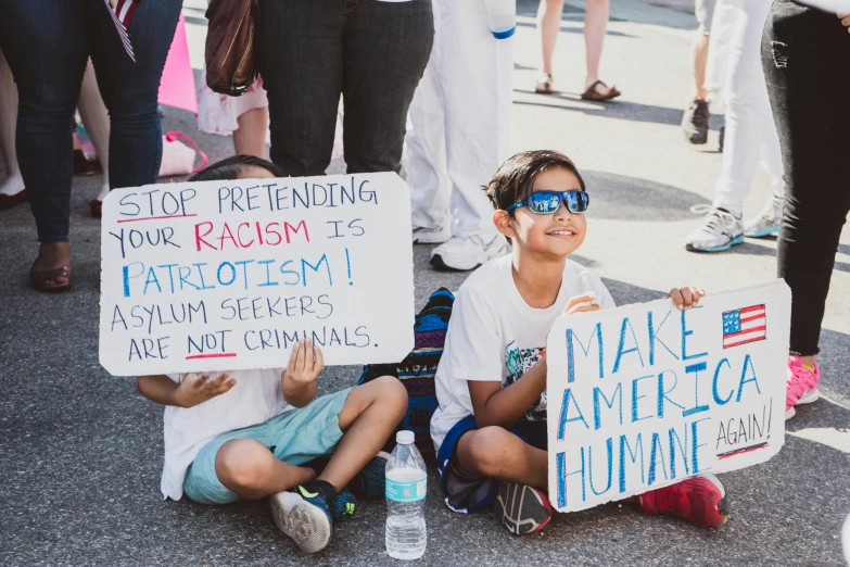 two young children sit outside holding up signs