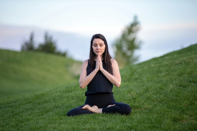 woman in black shirt doing yoga on grass hill
