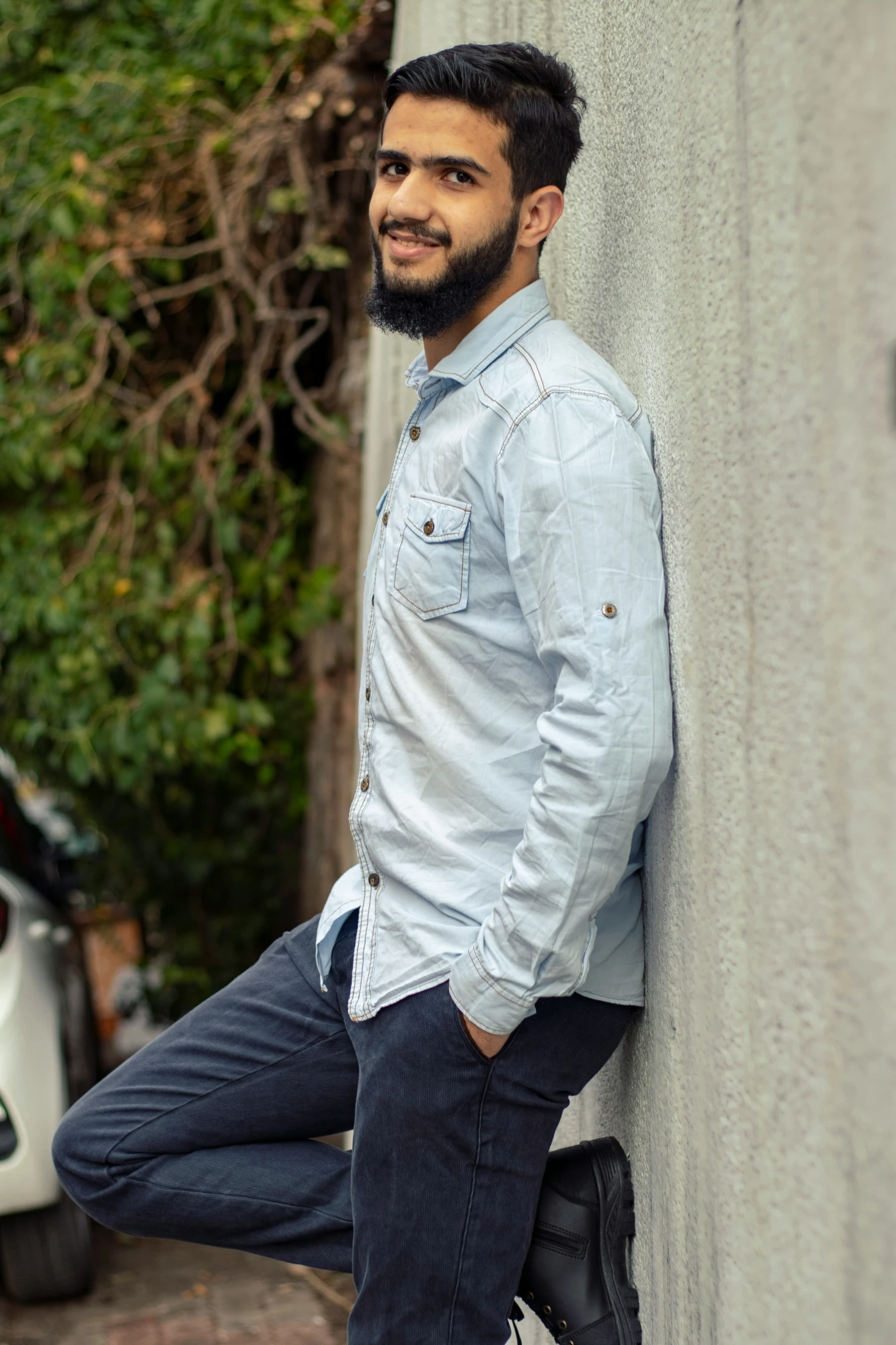 a bearded man leaning against the side of a building