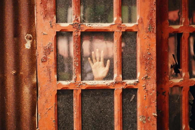 an old rusty metal window with hand and fingers on the window