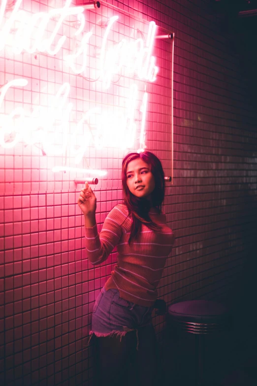 a young lady poses for the camera near a wall of pink tiles