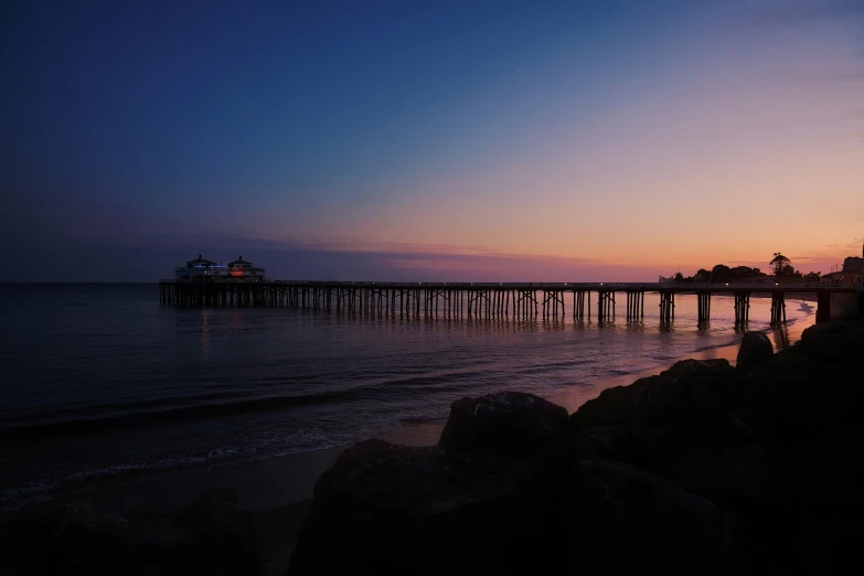 the sun sets over a beach and a pier