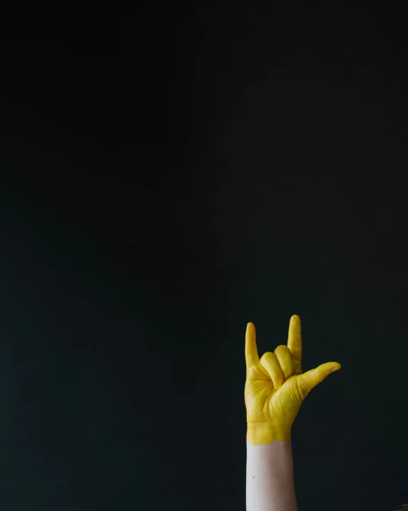 a person with yellow painted hand showing the sign peace