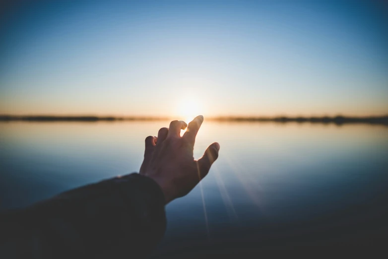 a person holding their hand out towards the sun