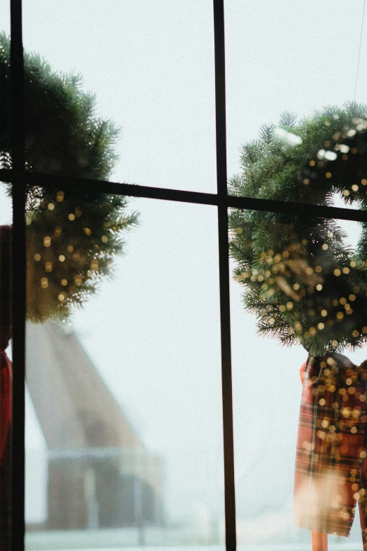 a couple holding christmas wreaths looking out of a window