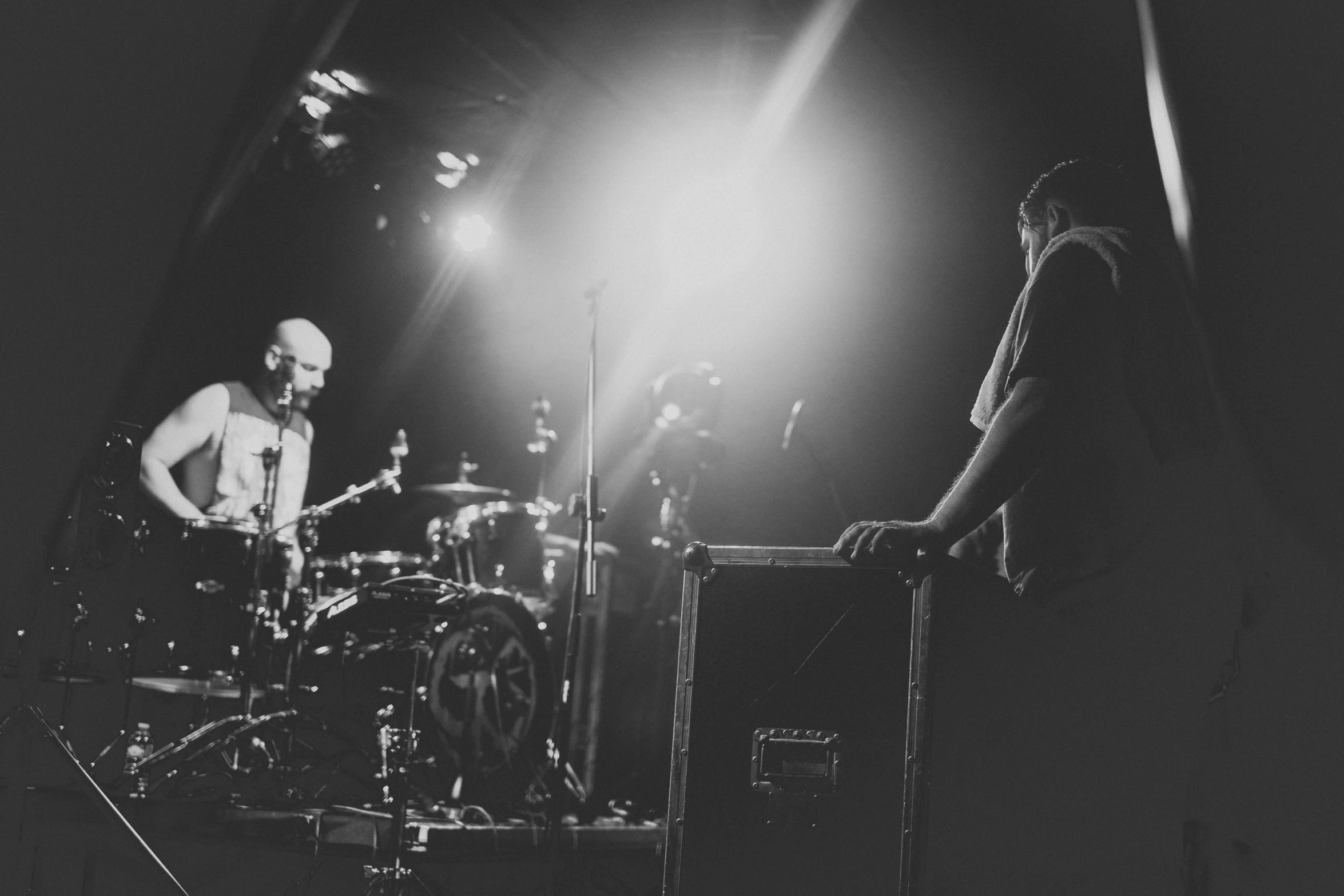two men are playing on the drum set while another man stands behind them