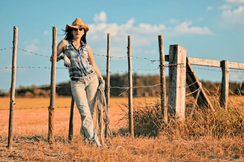 a girl in blue denim shirt and hat leaning against a fence