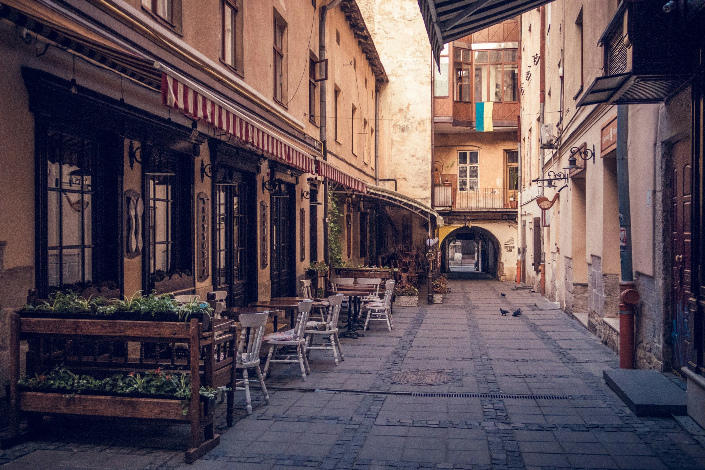 the outside of an alley way with tables and chairs lined up on either side