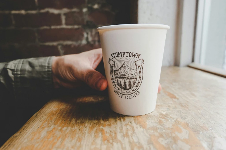 a person holding a cup on top of a wooden table