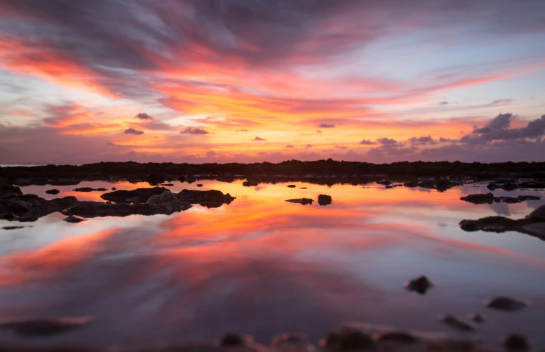 a sunset with pink clouds reflecting in the still water