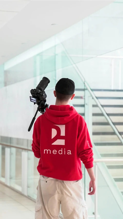 the back of a man in a red sweatshirt carrying a tripod