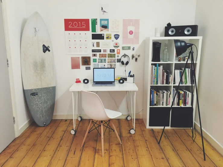 a room with a laptop and a surfboard on the wall